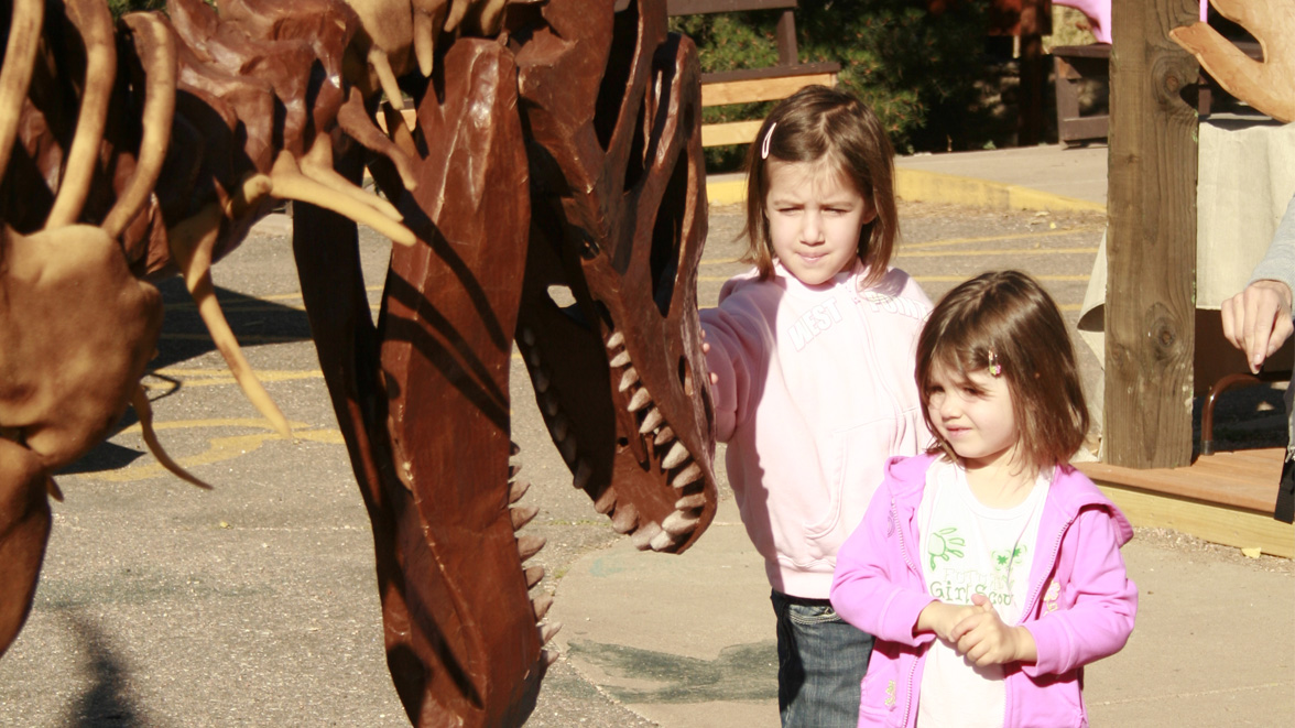 Two Girl Scouts interact with Mr Bones, a large puppet T. rex operated by puppeteer Tim Seeber