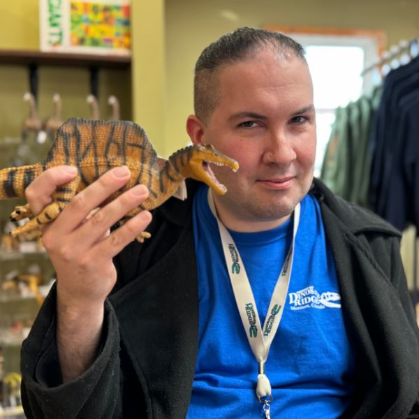 Photo of Ozan Youg holding a toy dinosaur in the gift shop.